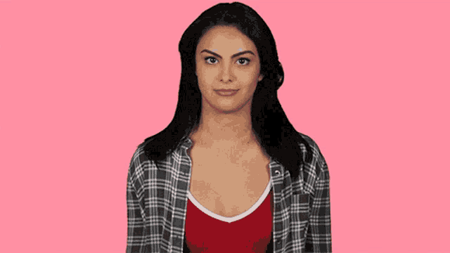 a woman wearing a plaid shirt and a red tank top smiles on a pink background