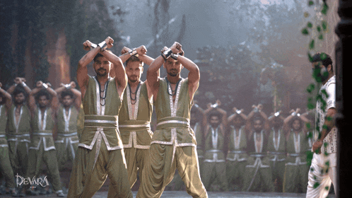a group of men are dancing in front of a sign that says " devara "