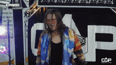 a woman in a colorful jacket stands in front of a sign that says cap