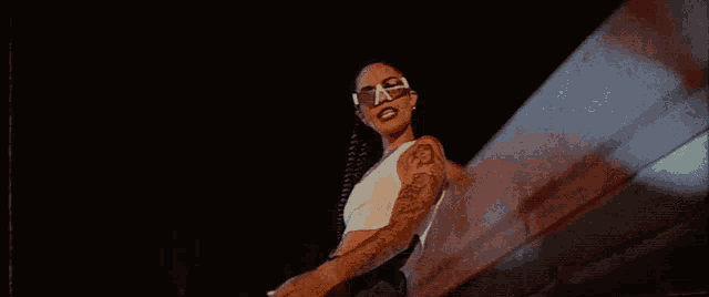 a woman wearing sunglasses and a white tank top has a tattoo on her arm