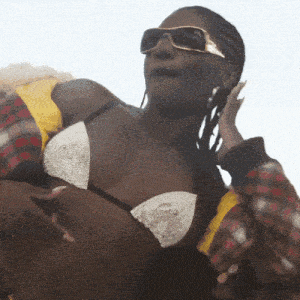 a woman wearing sunglasses and a bikini top holds her hand to her ear
