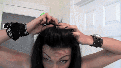 a woman wearing a bandana and a watch holds her hair up