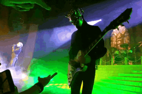 a man playing a guitar on a stage with a drum set in the background