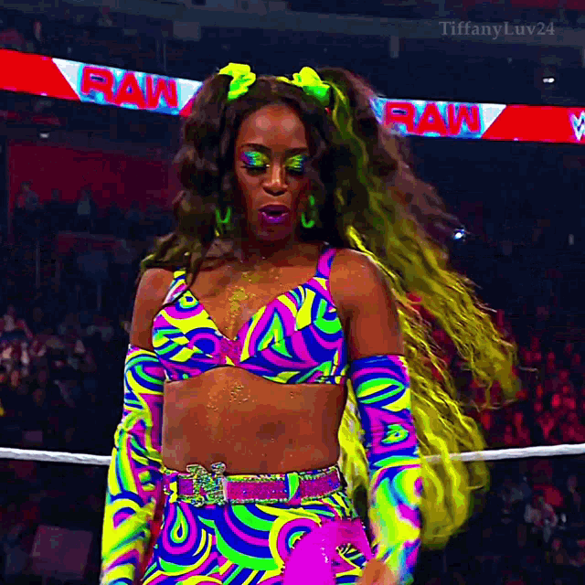 a woman in a colorful outfit is standing in a wrestling ring with a sign that says raw in the background