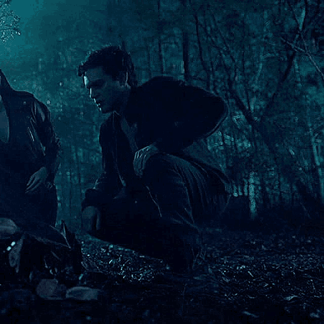 a man and a woman are kneeling down in the woods at night