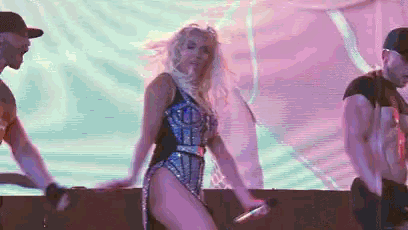 a woman is holding a microphone and dancing in front of a large screen