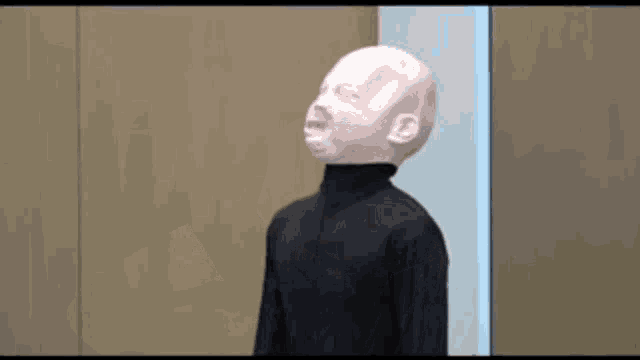 a mannequin with a white face and a black turtleneck is standing in a room .