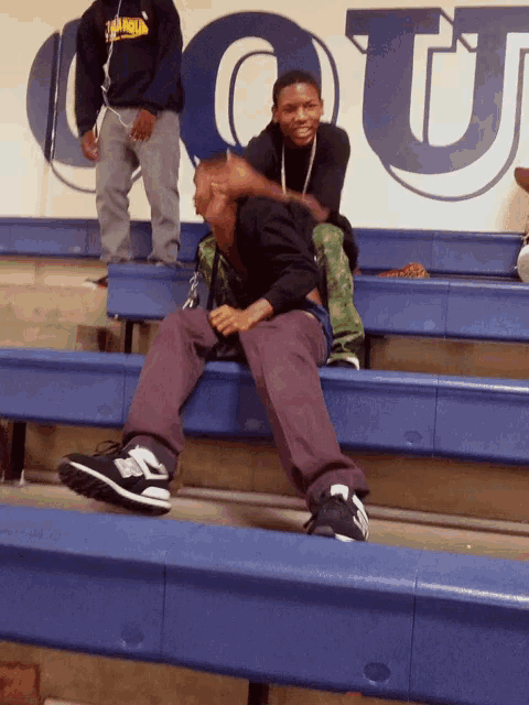 a boy wearing a hoodie that says ' kings ' on it sits on a blue bench