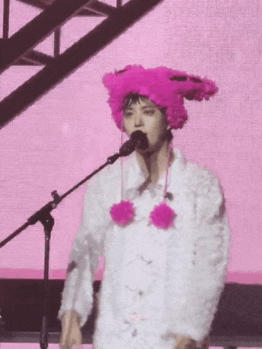 a person wearing a pink hat and a white coat is singing into a microphone