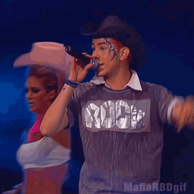 a man in a cowboy hat is singing into a microphone while a woman in a pink hat looks on