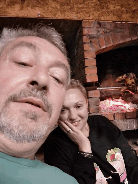 a man and a woman pose for a picture in front of a brick fireplace