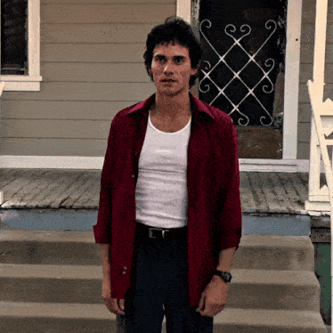 a man wearing a red shirt and a white tank top stands on a porch