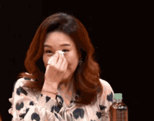 a woman wipes her face with a napkin while sitting in front of a bottle of water
