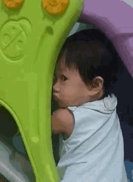 a baby is standing next to a green and purple toy .