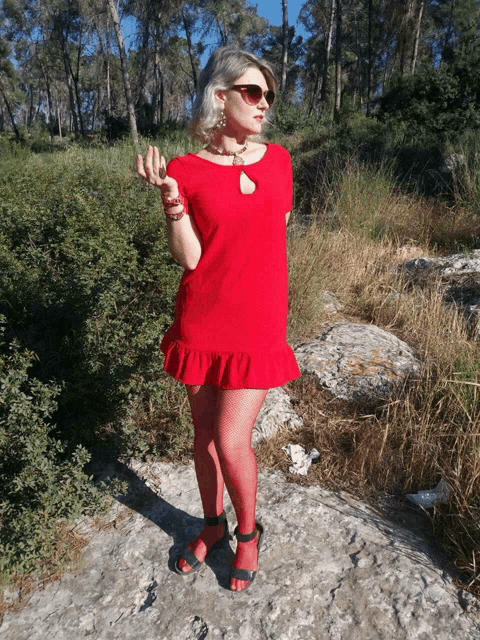 a woman in a red dress and red tights stands on a rock in the woods