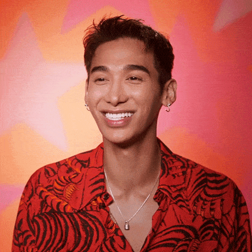 a young man wearing a red shirt and a silver necklace smiles for the camera