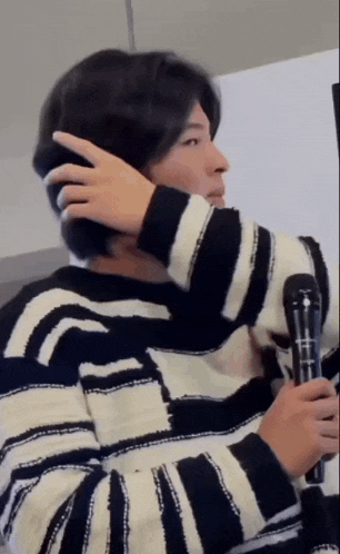 a man in a black and white striped sweater is holding a microphone and adjusting his hair .