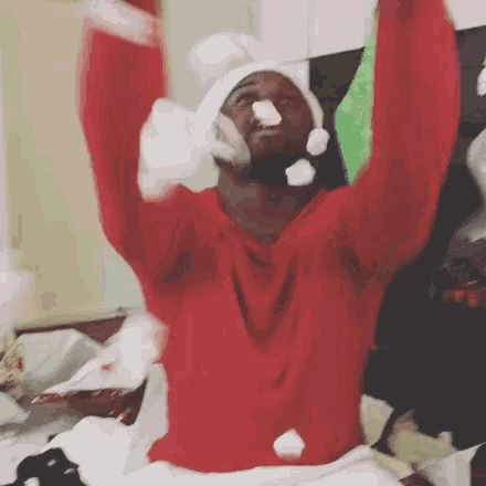 a man wearing a santa hat and a red sweater is sitting on a bed .