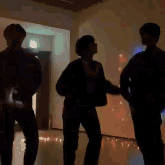 a group of people are dancing in a dark room with lights on the wall .