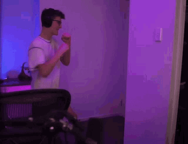 a young man wearing headphones and glasses is standing in a room with purple lights .