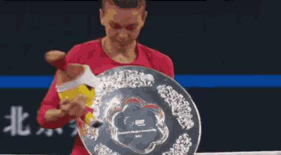 a woman in a red shirt is holding a silver trophy with a flower design on it