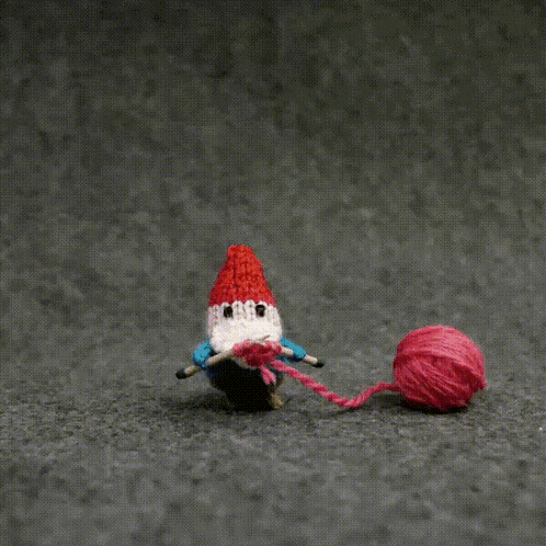 a crocheted gnome playing with a ball of yarn
