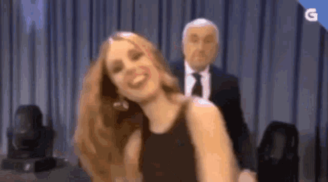 a woman is dancing on a stage with a man in a suit and tie behind her .
