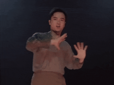 a young man in a gray shirt is dancing in a dark room .