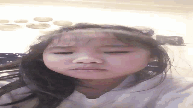 a little girl is making a funny face with her eyes closed .