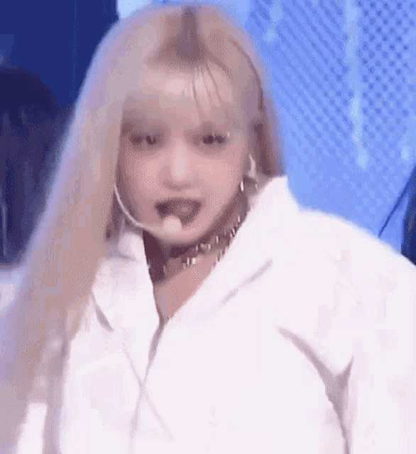 a close up of a woman with blonde hair wearing a white jacket and a microphone .
