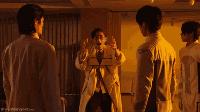 a group of men are standing in a room with the website dryedmangoez.com in the bottom right corner