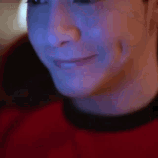 a close up of a person 's face with a red shirt on and a black collar .
