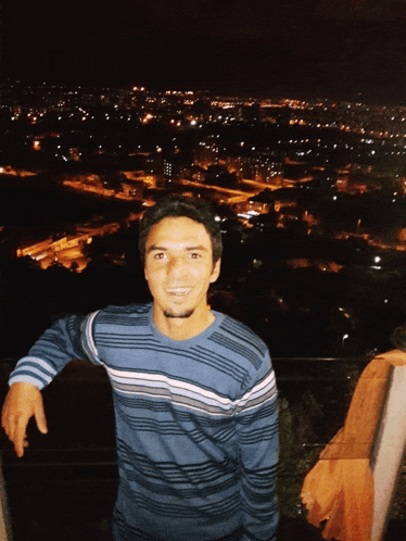 a man in a blue and white striped sweater stands in front of a city at night