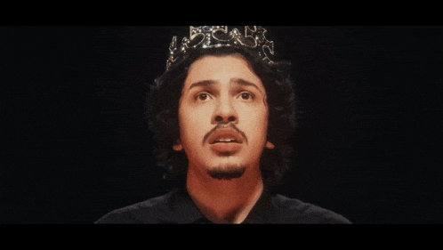 a man wearing a crown on his head looks at the camera