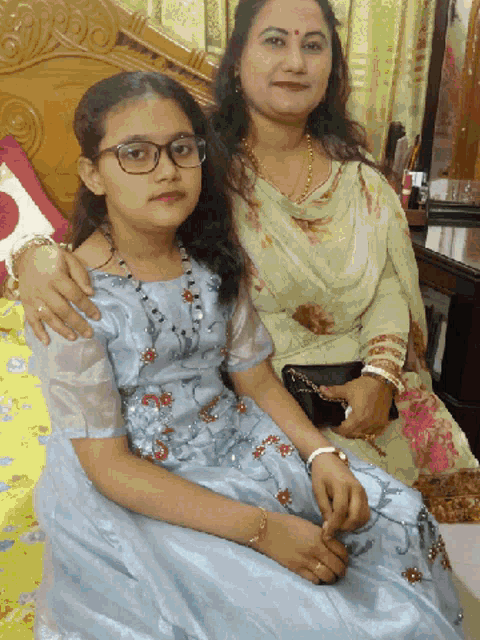 a woman sitting next to a girl wearing glasses and a blue dress