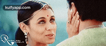 a woman with a red dot on her forehead looks at a man 's face