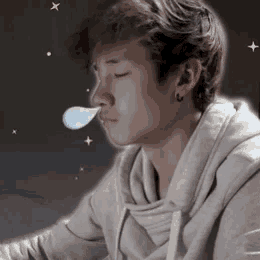 a young man is blowing a bubble out of his nose while wearing a hoodie .