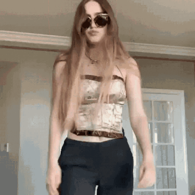 a woman with long hair and sunglasses is standing in a room .