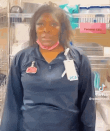 a woman wearing a blue shirt and a pink mask is standing in front of a shelf .