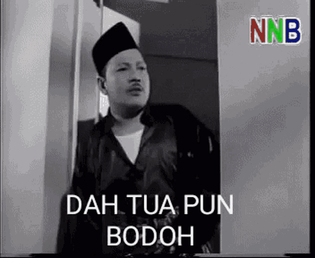 a black and white photo of a man standing in front of a door with the words dah tua pun bodoh .