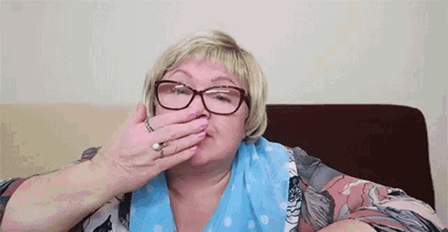 an elderly woman wearing glasses and a scarf is covering her mouth with her hand .