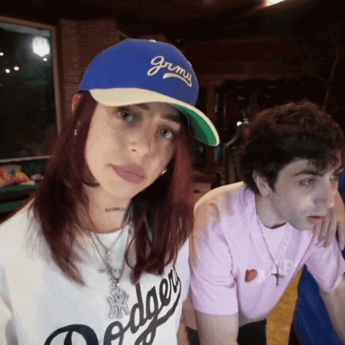 a woman wearing a dodgers shirt stands next to a man wearing a hat