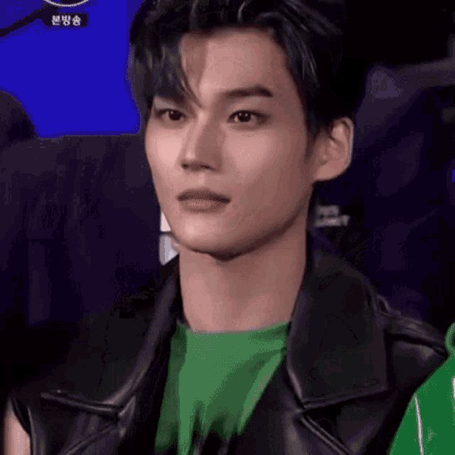a close up of a man wearing a green shirt and a black jacket .