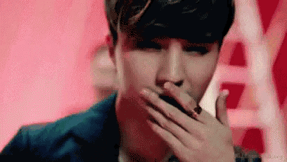 a young man is covering his mouth with his hand while smoking a cigarette .