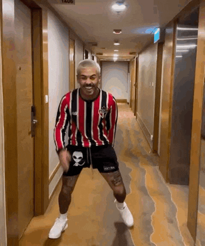a man in a striped shirt and shorts is dancing in a hotel hallway .