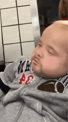 a baby is sleeping in a person 's arms while wearing a hoodie .