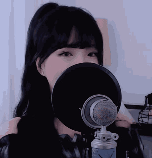 a woman stands in front of a microphone covering her face with a black shield