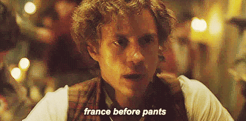 a man with curly hair is sitting at a table with the words france before pants written on the screen .