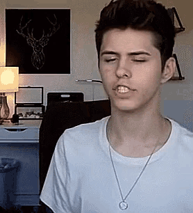 a young man wearing a white t-shirt and a necklace is making a face .