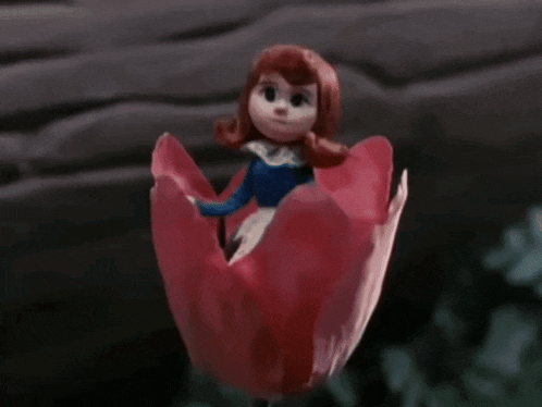 a doll is sitting inside of a red flower and waving .